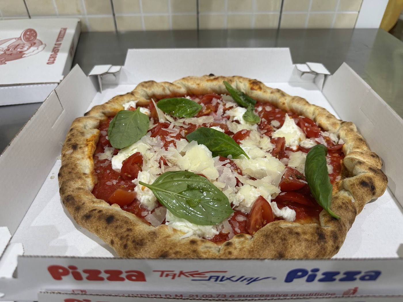 Pizza con pomodorini, mozzarella, basilico e scaglie di grana, nel cartone